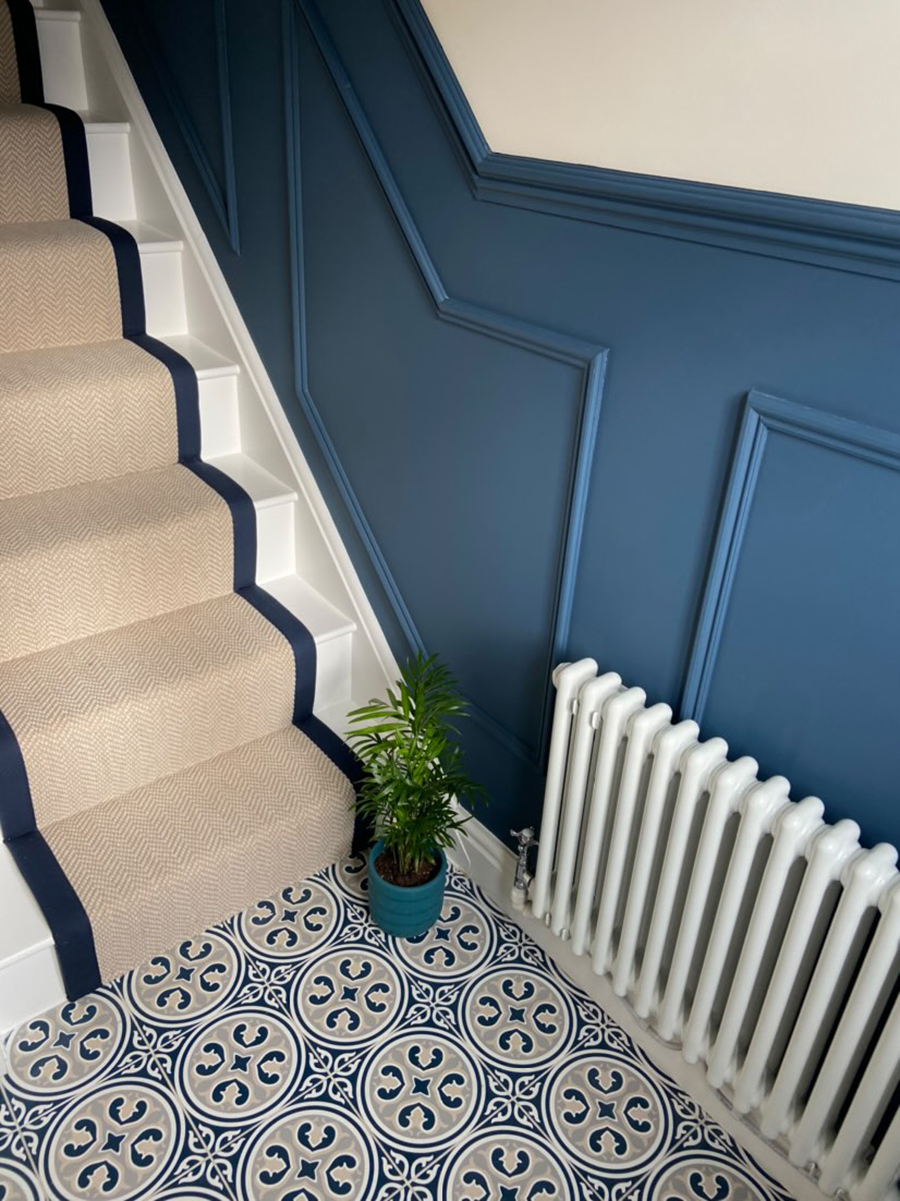navy hallway with panelling and navy Victorian tiles with a beige stair runner edged in navy